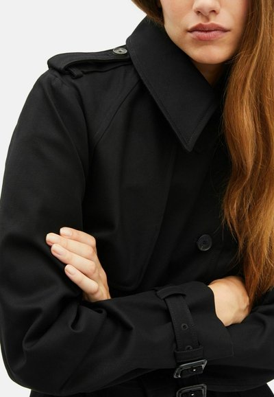 Czarny trenchcoat z wysokim kołnierzem, detalami z guzikami i akcentami w postaci paska. Materiał wydaje się gładki, z wyraźnie zarysowanymi rękawami i zwężającymi się mankietami.