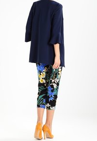 Marinblå tunika med utsvängda ärmar, matchad med svarta capribyxor med blommönster i blå, gula och gröna nyanser. Avslutad med orange klackar.