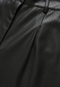 Tissu en cuir perforé noir avec une texture lisse, présentant des trous uniformément espacés. Conçu avec des plis pour ajouter de la forme.