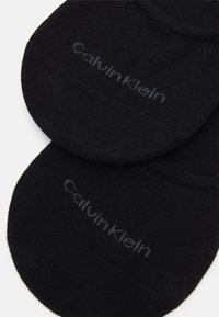 Chaussettes en coton noires avec une texture lisse et un design cut low. Présente le logo "Calvin Klein" en gris sur le côté.