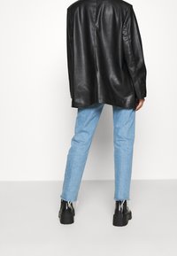 Sort læderblazer med en løs pasform, parret med lyseblå straight-leg jeans med frynset kant og sorte platformstøvler.