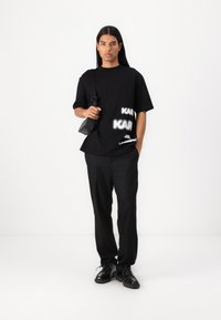 Μαύρο oversized t-shirt με λευκή υφασμάτινη εκτύπωση, μαύρο παντελόνι και μαύρα παπούτσια. Μικρή μαύρη ώμου τσάντα με κομψό, μινιμαλιστικό σχέδιο.