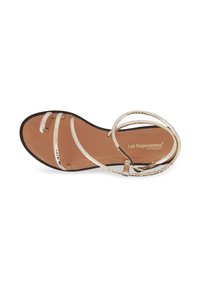 Women's sandal with a brown leather insole, featuring metallic gold straps that crisscross over the foot and a flat black outsole.