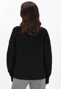 Schwarzer übergroßer Pullover mit strukturierter Oberfläche, geripptem Saum und fallenden Schulternähten. Die Rückansicht zeigt ein weiches, flauschiges Erscheinungsbild und eine lockere Passform.