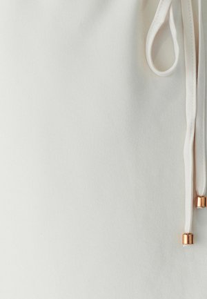 Bela tkanina z gladko teksturo, ki ima vrvico z metalnimi zlatimi poudarki. Oblikovanje poudarja preprostost in eleganco.