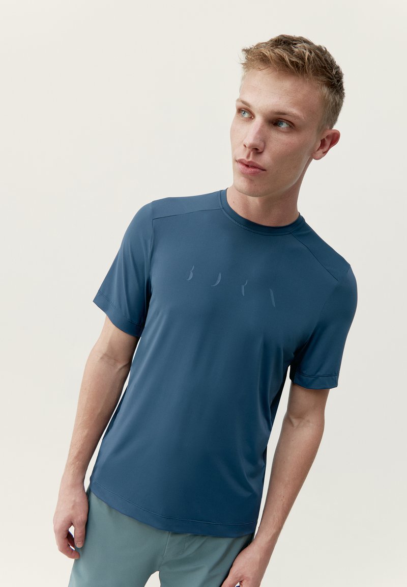 Krátký rukáv atletického trička ve tmavě modré látce s hladkou texturou a jemným logem na přední straně.