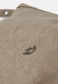 Beżowy materiał skórzany o teksturowym wykończeniu. Posiada małe metaliczne logo skrzydlatych serc. Proste, subtelne akcenty w designie.