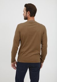 Brun langermet skjorte med rund hals, glatt tekstur og rett søm, kombinert med marineblå bukser. Minst sømmer og broderidetaljer.