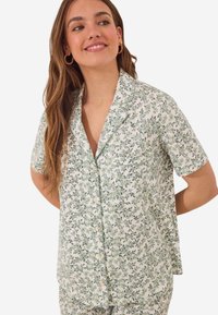 Ensemble de pyjama à manches courtes en blanc avec un motif de feuilles vertes et de fleurs, doté d'une coupe décontractée, d'un col et de boutons sur le devant. Tissu en coton doux.