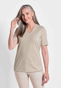 Beige V-Ausschnitt Kurzarmoberteil mit glatter, leicht glänzender Textur, kombiniert mit hellen Hosen. Auffällig durch sein einfaches und klassisches Design.