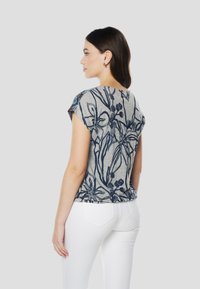 Pelēka ziedu T-krekls ar zilu botānisku rakstu, īsām piedurknēm un brīva piegriezuma. Valdāts kopā ar baltām biksēm, tai ir apaļa apkakle un aizmugurējs dizains.