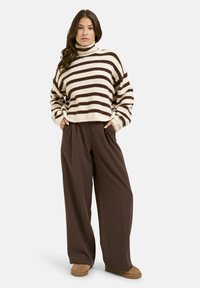 Striped, cropped sweater in beige and brown; relaxed-fit, high-waisted brown pants; worn with soft brown footwear.