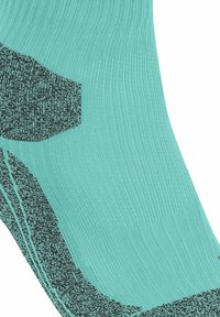 Turkusowa skarpetka sportowa z prążkowaną fakturą oraz czarnym wzorem na mankiecie i palcach, zapewniającym lepszą przyczepność.
