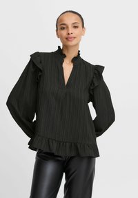 Blusa nera a maniche lunghe con righe verticali, collo e polsini arricciati, e un orlo svasato. Realizzata in un tessuto leggero e testurizzato.