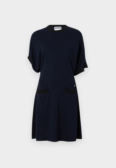 Robe en coton bleu marine avec des accents noirs, manches courtes, deux poches avant, col rond et un design décontracté. Détail en métal doré présent.