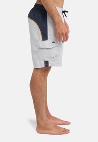 Ανδρικό μαγιό βερμούδα σε ανοιχτό γκρι με ναυτικά μπλε στοιχεία, ελαστική μέση, κορδόνι, πλαϊνή τσέπη και κίτρινα διακοσμητικά κατά μήκος των ραφών.