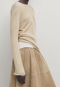 Pull en maille beige à manches longues, associé à une jupe en cuir suédé beige clair. Le pull présente une légère texture et une coupe décontractée.