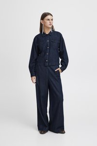 Σκούρα μπλε τζάκετ από τζιν με κουμπιά και δύο μπροστινές τσέπες, σε συνδυασμό με φαρδιά σκουρόχρωμα τζιν παντελόνια. Απλός, χωρίς διακοσμητικά σχεδιασμός.