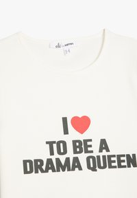 Beige Baumwoll-T-Shirt mit fettem schwarzen Text, der "Ich ❤️ SEIEN DRAMA QUEEN" sagt, und einem roten Herz-Graphic über dem Wort "Ich."