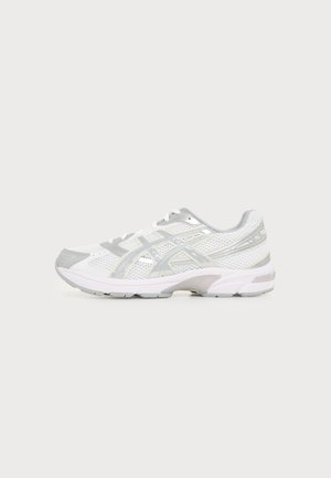 Baskets de sport blanches et grises avec tige en mesh, fermeture à lacets et semelle rembourrée, vues de profil sur un fond clair uni.