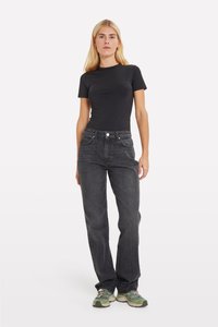 Top aderente a maniche corte di colore nero abbinato a jeans scuri a vita alta. La modella indossa sneakers verde chiaro con accenti colorati.