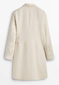 Manteau beige sur mesure à la longueur genou avec manches longues et col classique, présenté de dos sur fond blanc.