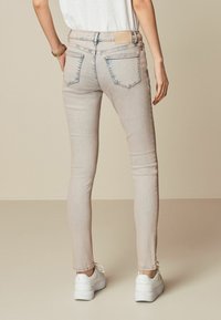 Svetlo bež skinny jeans hlače z dvema zadnjima žepoma, subtilnim blenšanjem in usnjenim etiketom na pasu, v kombinaciji z belimi športnimi copati.