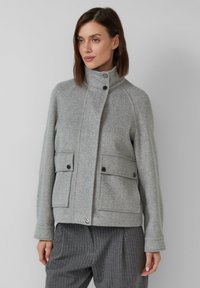 Grau meliertes Wollsakko mit hohem Kragen, zwei vorderen Taschen, Knopfverschlüssen und Detail an den Bündchen. Weiche Textur und taillierte Passform.