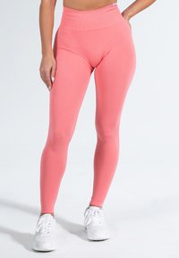 Leggings fucsia a vita alta realizzati in tessuto elasticizzato, con una texture liscia e una forma aderente, abbinati a scarpe da ginnastica bianche.