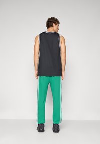 Sleeveless black athletic top with white trim paired with green sweatpants featuring white side stripes. Black athletic shoes complete the outfit.