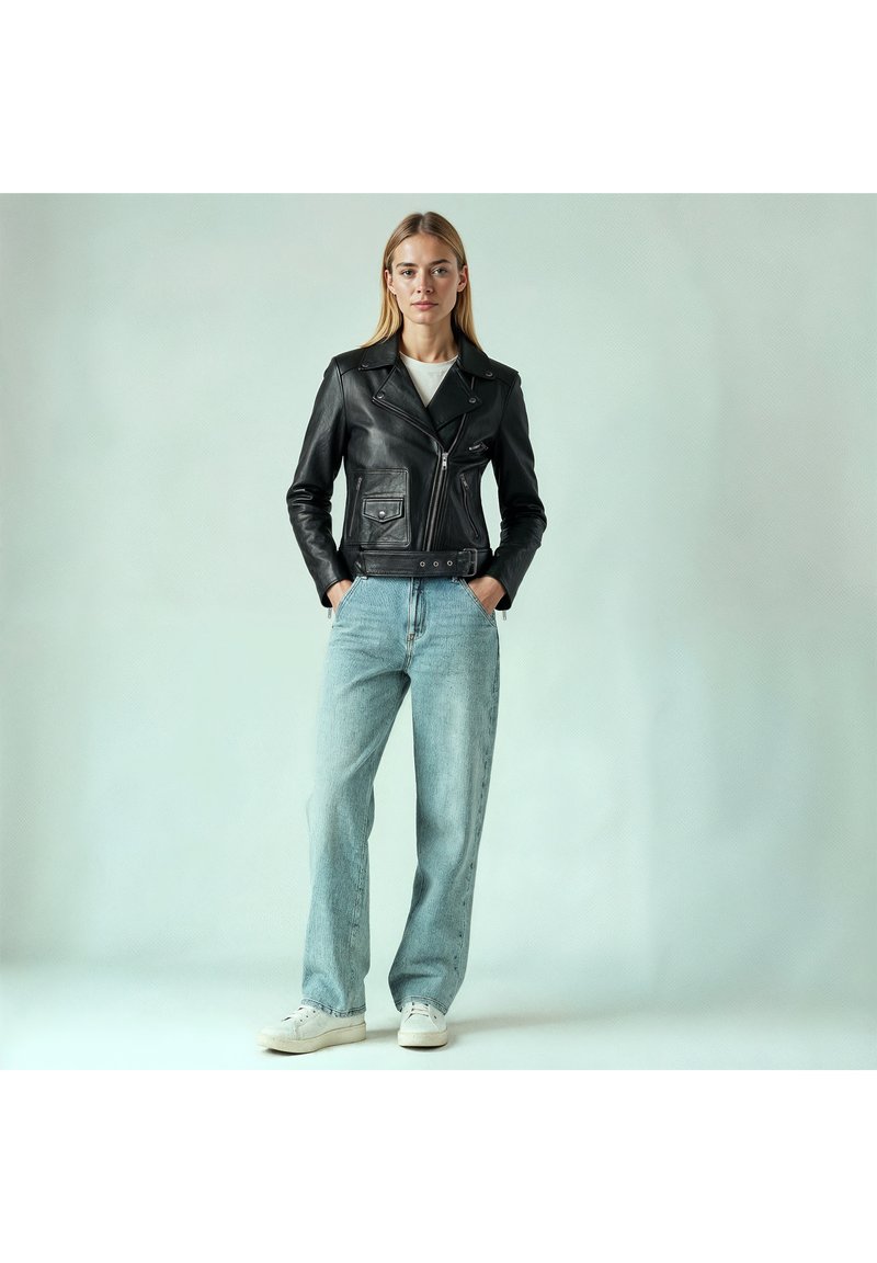 Schwarze Leder-Motorradjacke mit asymmetrischem Reißverschluss, zwei Fronttaschen, getragen über einem weißen Top, kombiniert mit hellblauen, weit geschnittenen Jeans und Sneakers.