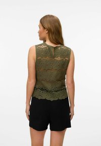 Top in pizzo verde oliva con motivo floreale, design senza maniche, dettaglio con apertura a chiave sul retro e orlo scallop, abbinato a pantaloni corti neri.