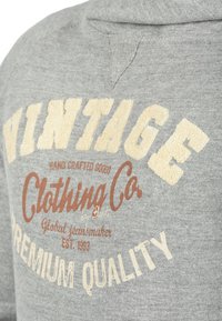 Gray sweatshirt featuring large, textured "VINTAGE" text in off-white and brown. Includes "Clothing Co" and "Premium Quality" text details.