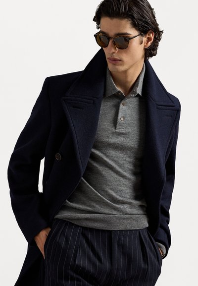 Tamsiai mėlynas vilnos mišinio paltas su plačiais atvartais, pilkas mezgimo polo ir dryžuotos kelnės. Papuošta vėžlio kiauto akinių nuo saulės.