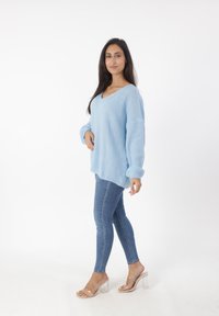Maglione lavorato a maglia blu chiaro con scollo a V e maniche lunghe, abbinato a jeans skinny e sandali con tacco trasparente. Texture morbida e vestibilità ampia.