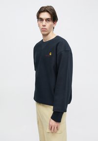 Μπλε ναυτικό φούτερ με μακριά μανίκια, στρογγυλή λαιμόκοψη και ραβδωτές μανσέτες. Διαθέτει μικρό κεντημένο λογότυπο στο αριστερό στήθος. Μαλακή υφή βαμβακιού.