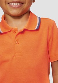 Pomarańczowa koszulka polo z teksturowanej tkaniny, z klasycznym kołnierzykiem, ozdobionym paskiem w kolorze granatowym i białym oraz dwoma dopasowanymi guzikami.