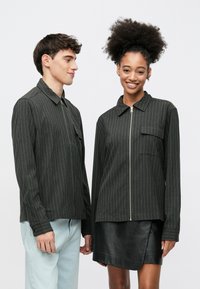 Paskiowane ciemnoszare kurtki z tkaniny mieszanej z bawełną; jedna posiada zamek błyskawiczny i kieszeń, druga kołnierzyk i mankiety na guziki.