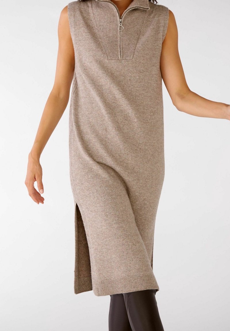 Robe en tricot sans manches beige avec un col zippé haut, une fente sur le côté et des détails côtelés au niveau du cou et de l'ourlet, dotée d'un tissu doux et texturé.
