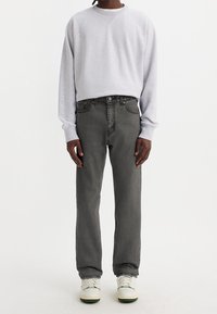 Sudadera gris con mangas raglán, combinada con jeans negros de cintura alta. El modelo lleva zapatillas blancas con detalles en verde.