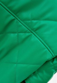 Prošívaná zelená kožená tkanina s viditelným šitím, s hladkým povrchem a diagonálním švem. Měkká a živá barva.