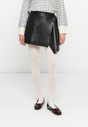 Donna che indossa una mini gonna in pelle nera asimmetrica, collant bianchi, ballerine bordeaux con fiocchi e un maglione a maniche lunghe a fantasia.