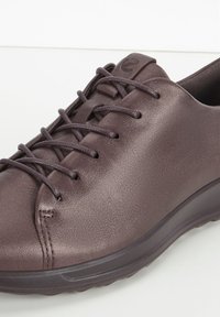 Sneaker in pelle viola scuro con punta arrotondata, superficie testurizzata e chiusura con lacci. Presenta una suola a profilo basso e un branding minimale.