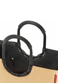 Tan woven fabric tote with black textured circular handles and zipper pocket. Features a contrasting color accent on the side.