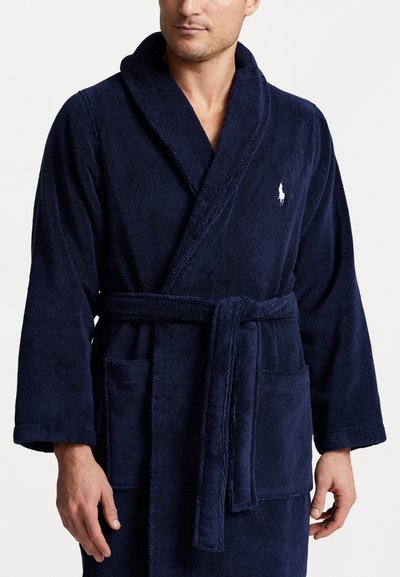 Bata de baño de rizo azul marino con cuello chal, mangas largas, cinturón de lazo y dos bolsillos frontales. Presenta un logo bordado en el pecho.