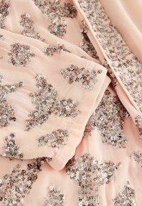 Tissu rose clair avec des sequins argentés dispersés cousus en motifs floraux et abstraits.