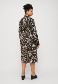 Robe à manches longues avec un motif abstrait noir et beige, réalisée en tissu léger, dotée d'un col montant et d'une silhouette droite.