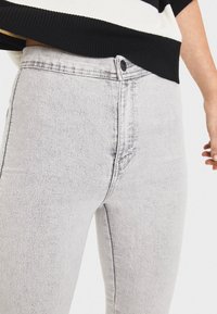 Ljusgrå denimjeans med hög midja, minimal blekning och en subtil textur. Återfinns med standardknapp och dragkedjestängning.
