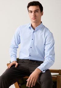 Chemise bleu clair à motif fin, col boutonné et boutons foncés, assortie à un pantalon à fines rayures foncé.