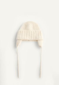 Zimná čiapka smotanovej farby s ušnými klapkami a dlhými vrkočmi, zobrazená na bielom pozadí.